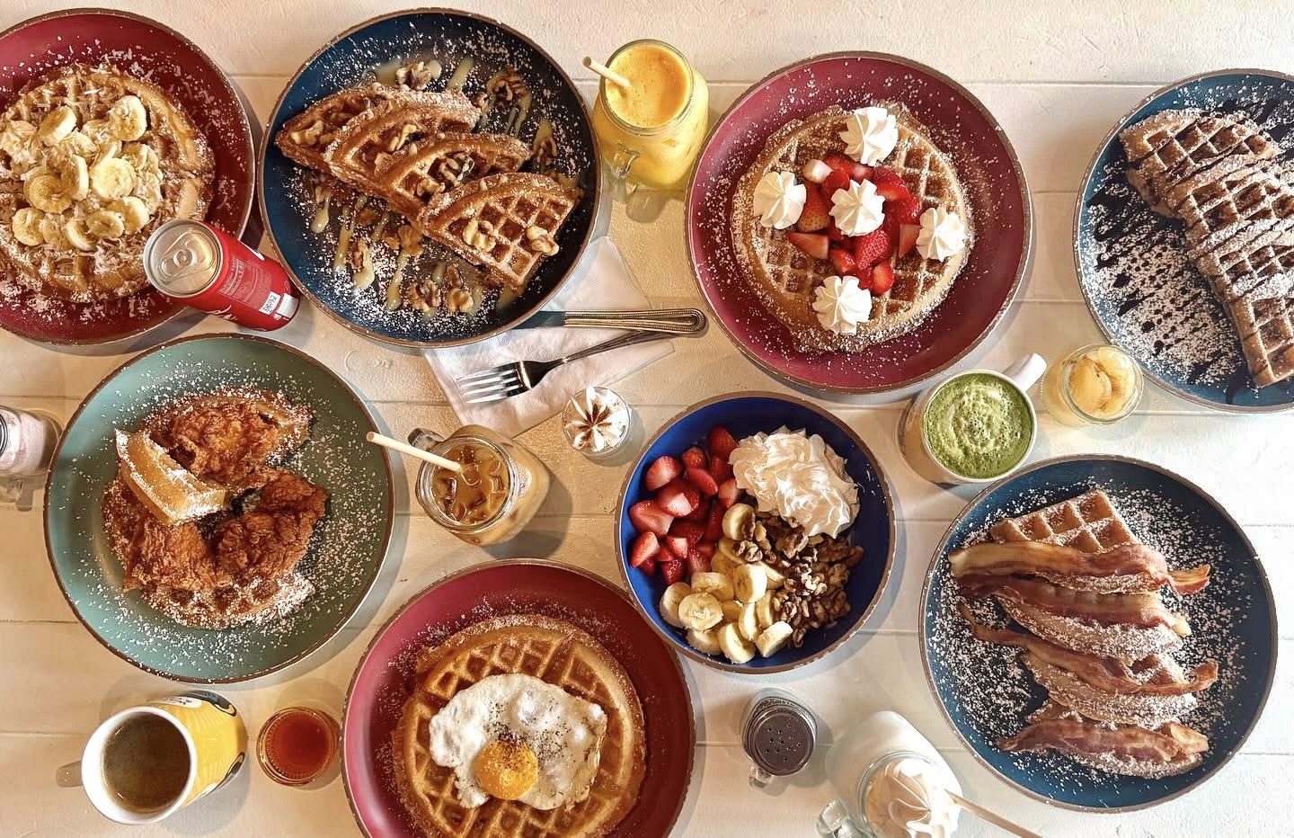 A table spread of Waffle Monkey waffles at the Sarasota cafe — banana, fruit and chocolate waffles, chicken and waffles, a bacon waffle and a fruit bowl, with Costa Rican coffee